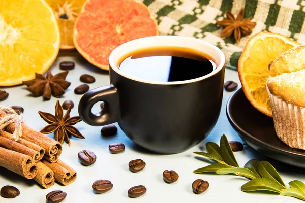 A mug of black coffee on a table with a cupcake napkin and cinnamon scattered coffee beans and sliced orange slices
