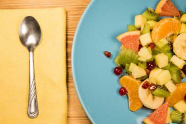 Bir peçete, kaşık ve yazıt, boşaltmak için yer ile ahşap bir masa üzerinde duran mavi plaka narenciye taze meyve salatası