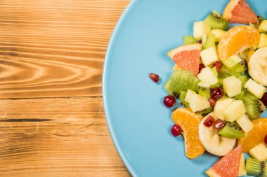 Narenciye yazıt için bir yer ile ahşap bir masa üzerinde duran mavi plaka ile taze meyve salatası.