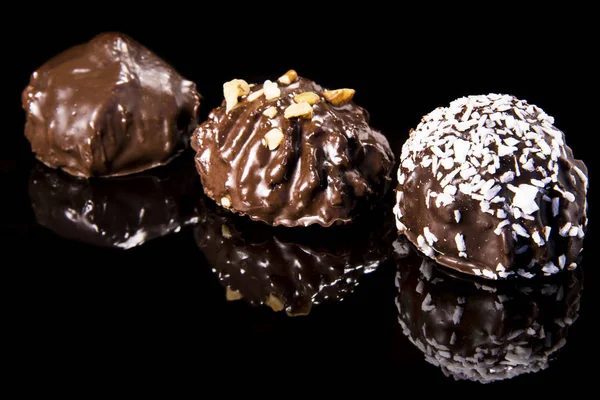 Tres pasteles de chocolate en una superficie de espejo negro espolvoreado con chips de coco y avellana, caramelo de chokolate oscuro — Foto de Stock