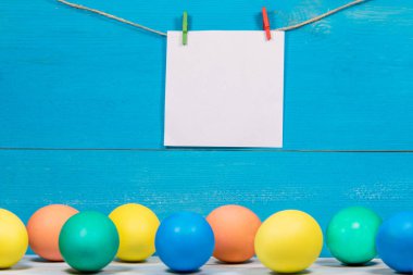 Paskalya yumurta beyaz kağıt üzerinde yazıt için yer ile mavi arka plan üzerinde farklı renklerde boyanmış