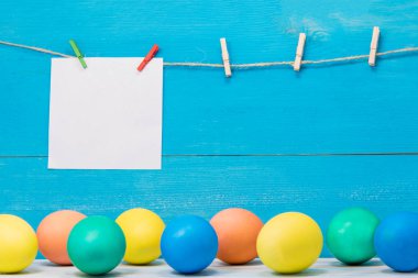 Paskalya yumurta beyaz kağıt üzerinde yazıt için yer ile mavi arka plan üzerinde farklı renklerde boyanmış