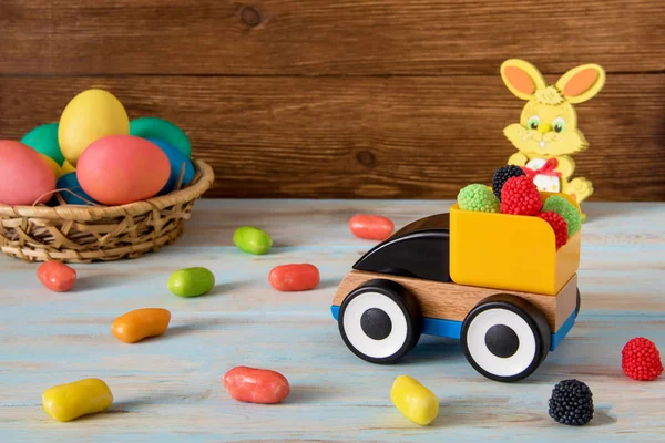 Easter toy car with color sweets and Easter eggs on wooden background — Stock Photo, Image