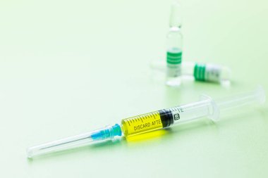 İlaç masasındaki küçük şişe ve şırınga açık yeşil arka planda koronavirüs aşısı için hazır.