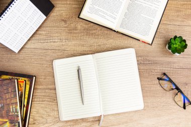 Okul ve eğitim alanına geri dön. Boş not defteri, cam, kalem, yeşil bitki ve ataç yığınlı eski ahşap masa masası, düz konsept, fotokopi alanı olan üst görünüm.