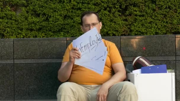 Безробітна людина на вулиці з кортоном з написами потребує роботи. Зневірений чоловік сидить на бетонній міській вулиці з коробкою з особистими речами . — стокове відео