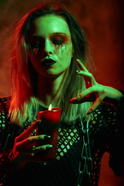 Zbliżenie portret pięknej seksownej czarownicy z makijażem halloween. czerwone i czarne malowanie twarzy.Świeca w rękach — Zdjęcie stockowe