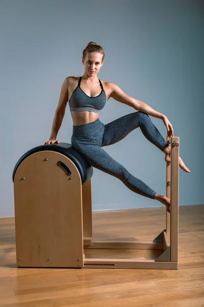 Bella donna bionda positiva è in fase di preparazione l'esecuzione di esercitazione pilates, formazione su attrezzature botte. Concetto di fitness, attrezzi fitness speciali, stile di vita sano, plastica. Copia spazio, sport — Foto Stock