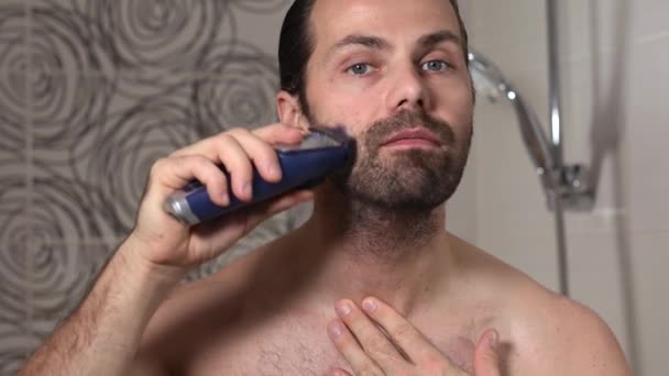 Stilig ung man med långt hår rakar skägget med en trimmer i badrummet. Närbild. — Stockvideo