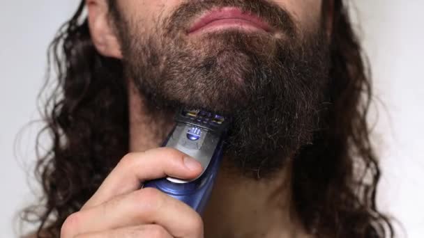 Uzun saçlı yakışıklı genç adam banyoda tıraş makinesiyle sakalını tıraş ediyor. Yakın plan.. — Stok video