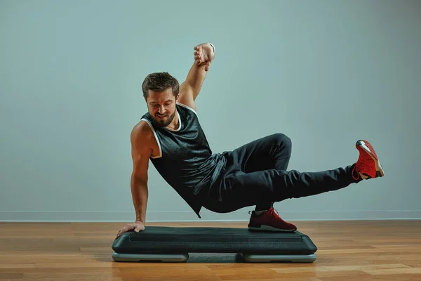 Muskulöser junger Mann beim Training auf Trittbrettern vor grauem Hintergrund im Studio — Stockfoto