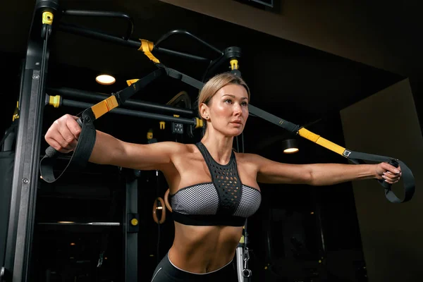 Első nézet magabiztos fiatal szőke nő csinál súlyemelés edzés Vonzó fiatal nő emelő súlyzók előre Erős képzett test alakja karok mellkas lábak. — Stock Fotó