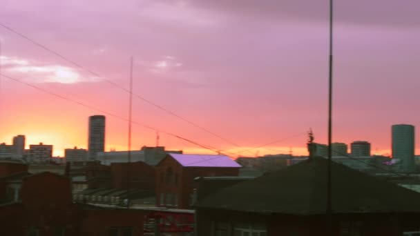 美しいオレンジ色の空と紫色の夕日の雲が町の傾斜屋根の上を移動します。4k夜. — ストック動画