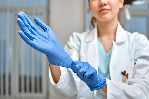 Close up de um médico feminino colocando um luvas de látex azul em um fundo de clínica . — Fotografia de Stock