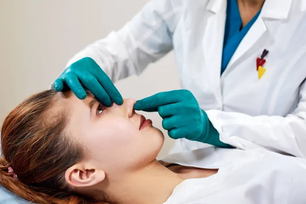 Κυρία με γύψο στην μύτη, ο γιατρός εξετάζει ασθενείς πρόσωπο μετά από πλαστική χειρουργική επέμβαση — Φωτογραφία Αρχείου