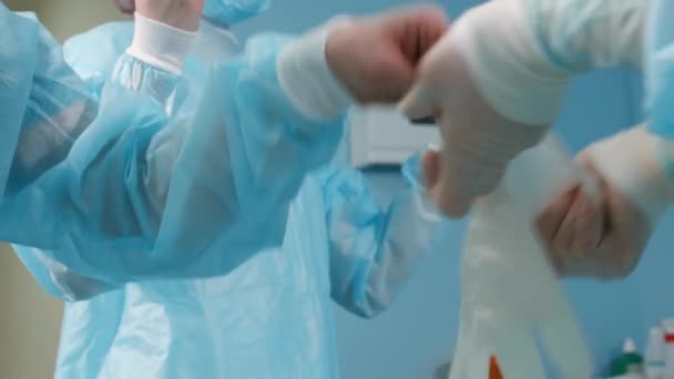 Asistente médico con una bata quirúrgica azul se pone guantes de látex en preparación para una cirugía . — Vídeos de Stock