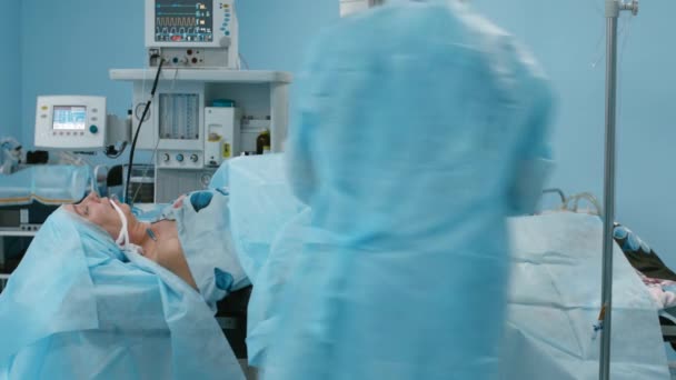 Patiente couchée sous anesthésie attachée à la table chirurgicale, le chirurgien et l'assistante préparent le patient et prennent des dispositions pour la stérilité dans la salle d'opération — Video