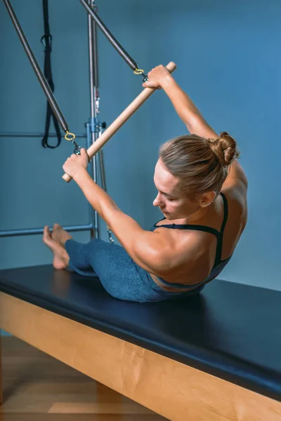 Young girl doing pilates exercises with a reformer bed. Beautiful slim fitness trainer on reformer gray background, low key, art light. Fitness concept — Stock Photo, Image