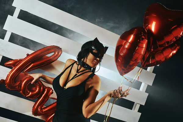 Sexy vrouw met grote borsten dragen van een zwart masker Paashaas staan op een zwarte achtergrond met hartvormige ballonnen en een liefde teken en ziet er zeer sensueel — Stockfoto