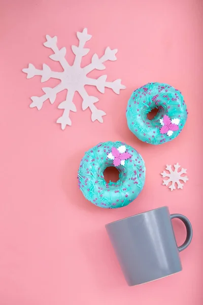 Blaue Donuts mit Zuckerguss und Kaffeetasse und Schneeflocken auf pastellrosa Hintergrund. süße Donuts. — Stockfoto