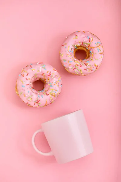 Donuts roses avec glaçage et tasse de café sur fond rose pastel. Doux beignets . — Photo