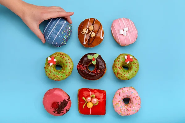 Various colorful donuts on blue background, female hand takes a donut. Top view. — Stock Photo, Image