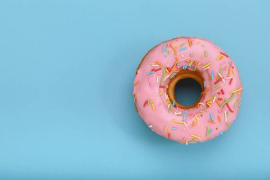 Pink donut on a blue background, top view, concept of desserts, pink color on blue. Copy space, blue background. clipart