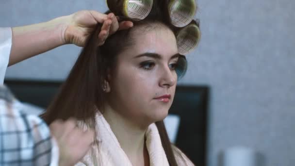 Makeup artist works as a stylist with a model. hairdresser makes hairstyle model. The hairstyle creates volume on the hair of the model using a comb. Winds hair curlers, makes a voluminous hairstyle. — ストック動画