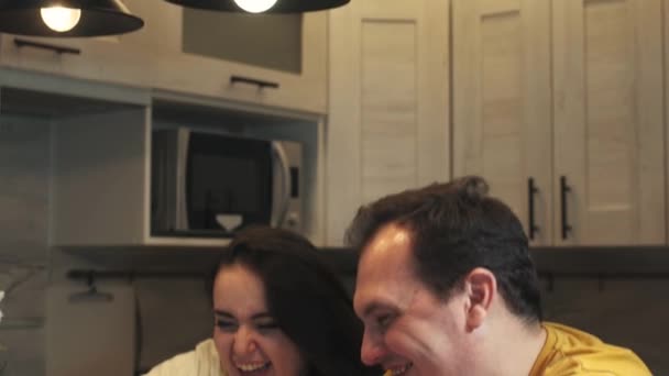 Cabeza tiro feliz familia pareja sentada en la mesa de madera en la cocina, utilizando teléfonos inteligentes, compartir aplicaciones o contactos. Sonriendo cónyuges casados jugando juegos móviles en línea, comprobando las redes sociales . — Vídeos de Stock
