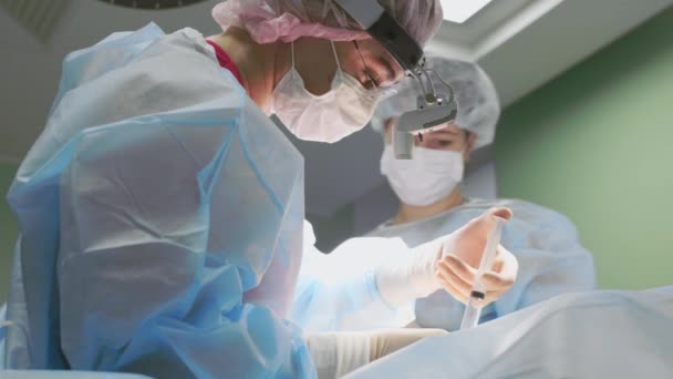 Kirurgisk team under operationen. Kirurger arbejder som et venligt team, fagfolk i den blå moderne operationsstue. Teamwork, rigtig operation, blåt lys. Plastikkirurgi, nærbillede, sundhed . – Stock-video