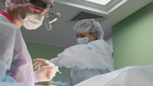 Zespół chirurgiczny podczas operacji. Chirurdzy pracują jako przyjazny zespół, profesjonaliści na niebiesko nowoczesnej sali operacyjnej. Praca zespołowa, prawdziwa operacja, niebieskie światło. Chirurgia plastyczna, zbliżenie, zdrowie. — Wideo stockowe