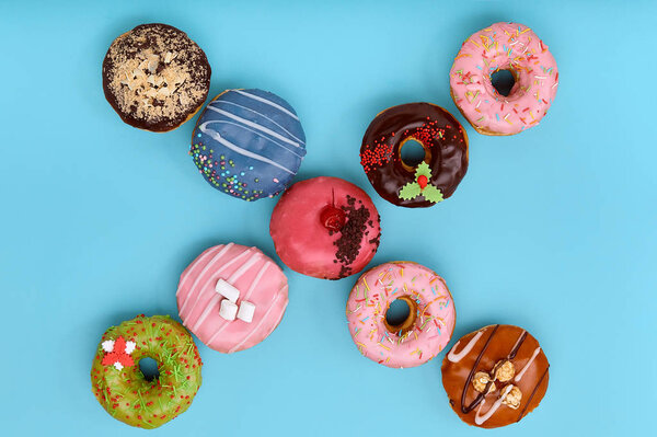 Sweet colored donuts on a blue background, laid out in the form of various geomitric figure, arrow, square, line, triangle, top view. Desserts, game of colors, blue background.