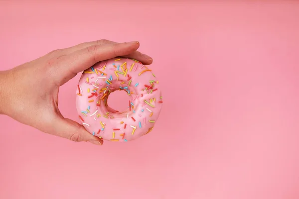 Weibliche Hand hält köstlichen Donut auf rosa Hintergrund, Nahaufnahme — Stockfoto