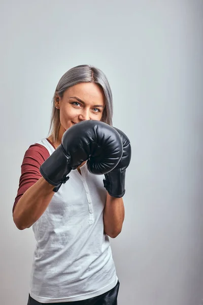 Joven hermosa boxeadora sexy posando con guantes de boxeo negro en sus manos sobre un fondo gris. Copiar espacio, fondo gris, logro de objetivos . — Foto de Stock