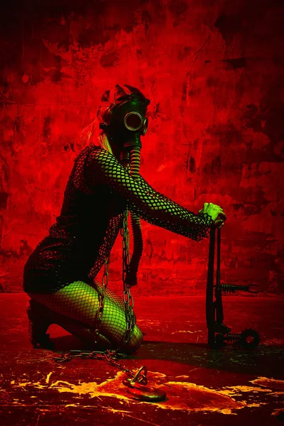 Modèle féminin en tenue Halloween avec masque à gaz posé sur un fond rouge. Magnifique fille en vêtements post-apocalypse célèbre le jour des morts. Concept d'Halloween, costume de sorcière, couleurs vives — Photo