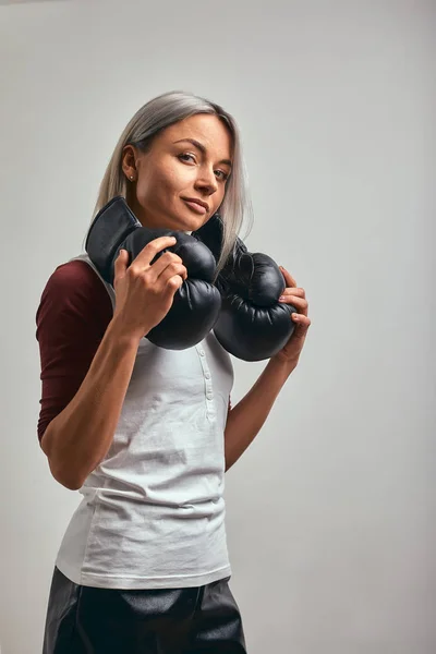 Joven hermosa boxeadora sexy posando con guantes de boxeo negro en sus manos sobre un fondo gris. Copiar espacio, fondo gris, logro de objetivos . — Foto de Stock