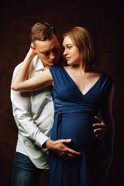 Pareja embarazada posando para la cámara sobre un fondo marrón, de tono bajo. Concepto de embarazo de moda. Copiar espacio, fondo marrón . — Foto de Stock