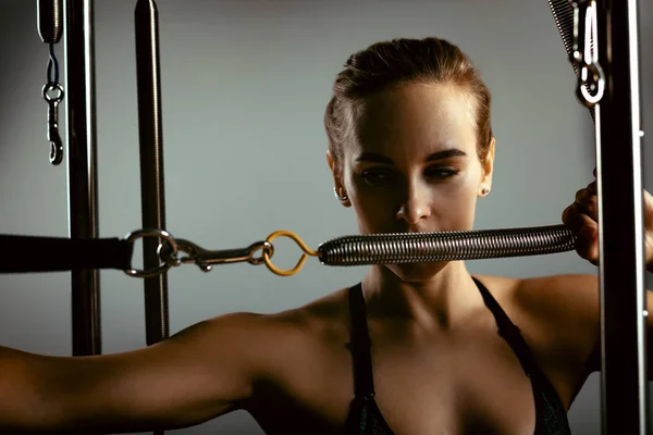 Chica joven haciendo ejercicios de pilates con una cama reformadora. Hermoso entrenador de fitness delgado sobre fondo gris reformador, bajo llave, luz de arte. Concepto Fitness — Foto de Stock