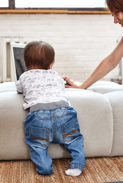 A woman with a child at a laptop sitting on a sofa. Work at home, freelancer, work during maternity leave for remote access.