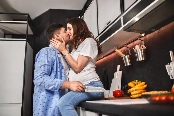 Sonriendo hermosa mujer embarazada y hombre en la cocina beber café y cocinar. Esperando una nueva vida, embarazo . — Foto de Stock