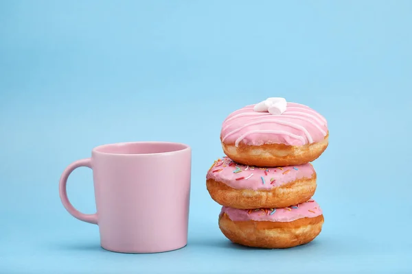 Süße rosa Donuts mit rosa Becher auf blauem Hintergrund. Konzept Dessert, süßes Leben, wir sind, was wir essen. Blauer Hintergrund, Kopierraum. — Stockfoto