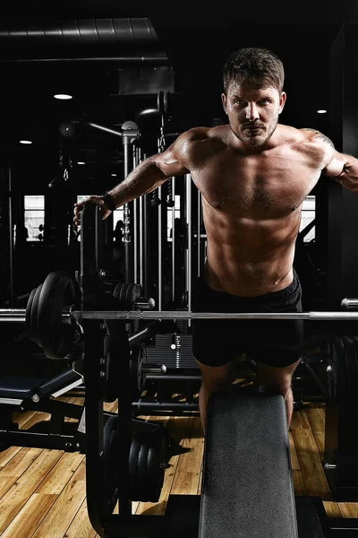 Un joven musculoso levantando un banco de pesas en el gimnasio. Hermoso cuerpo, logro de objetivos, el deporte como una forma de vida . — Foto de Stock