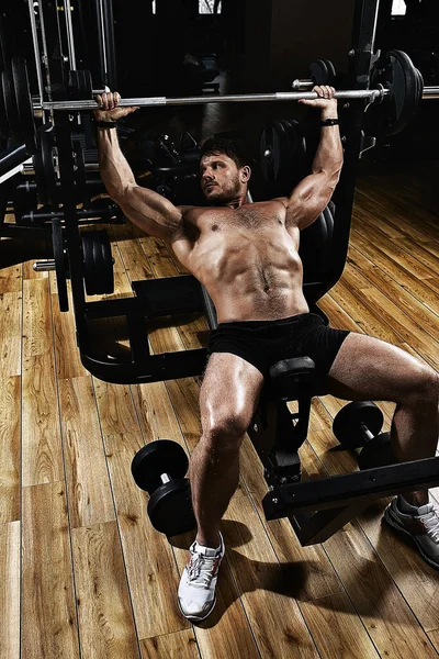 Young muscular man lifting a barbell bench press in the gym. Beautiful body, goal achievement, Sport as a way of life.