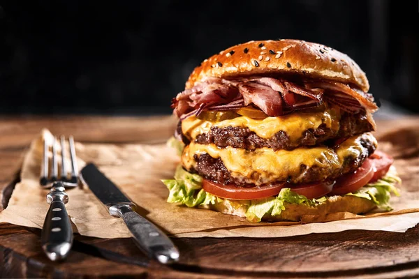 Čerstvý a šťavnatý hamburger na papírovém polštáři s pivem na dřevěném stole. Tmavé pozadí, tradiční americké jídlo. Nezdravé jídlo,... — Stock fotografie