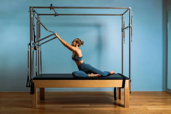 Young girl doing pilates exercises with a reformer bed. Beautiful slim fitness trainer on reformer gray background, low key, art light. Fitness concept — Stock Photo, Image