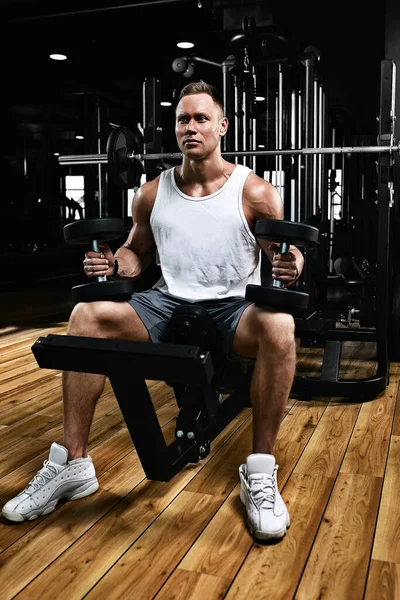 Muscular guy bodybuilder doing exercises with dumbbells in the gym. Athletic body, healthy lifestyle, fitness motivation, body positive.