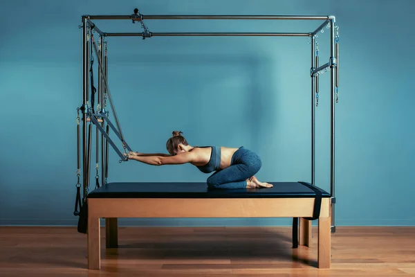 Genç bir kız ıslah yatağıyla pilates egzersizi yapıyor. Reformist gri arka planda güzel ince fitness antrenörü, sade anahtar, sanat ışığı. Fitness konsepti — Stok fotoğraf