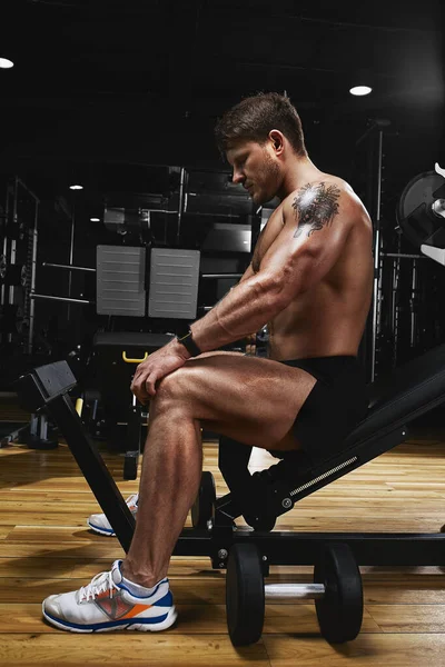 一个英俊的健美健美运动员用哑铃做运动的服装。健康的肌肉身体在黑暗的背景下.健康的生活方式. — 图库照片