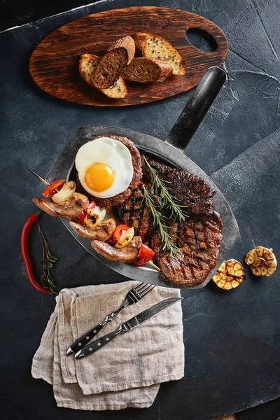 Bandeja de carne asada. Surtido de deliciosa carne a la parrilla con verduras. Carne mixta a la parrilla con salsa de pimienta y verduras. Chefs manos esparcir carne en un plato — Foto de Stock