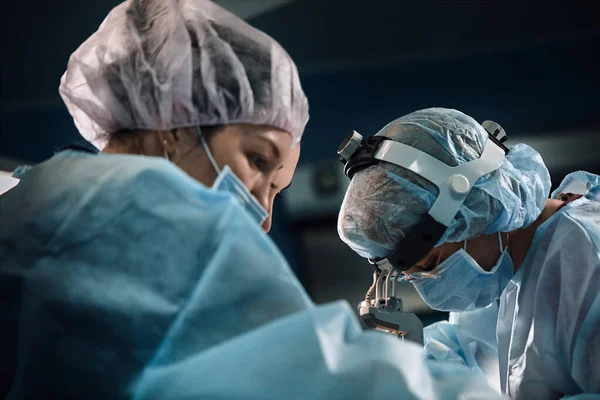 Equipo quirúrgico en quirófano, de cerca. Un equipo internacional de médicos profesionales en un quirófano moderno se somete a cirugía. Salvando vidas, medicina moderna, luz azul — Foto de Stock